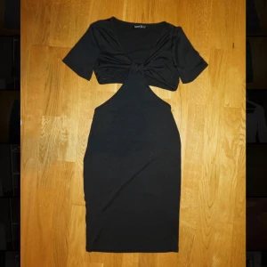 Svart cut out klänning med kort ärm - Svart kortklänning från med cool cut out-detalj framtill och twistad byst. Klänningen har korta ärmar och en tight passform som framhäver figuren. Perfekt för dig som vill sticka ut med en trendig look.