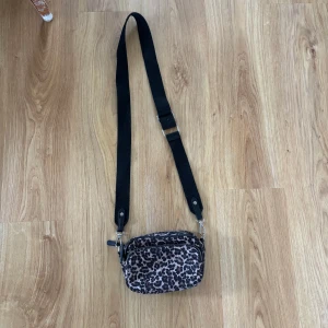 Leopardmönstrad axelväska med dragkedja - Cool axelväska med leopardmönster och bred svart justerbar rem. Väskan har två stora fack med dragkedjor och är perfekt för att bära det viktigaste. Materialet är mjukt och lätt, och designen sticker verkligen ut.