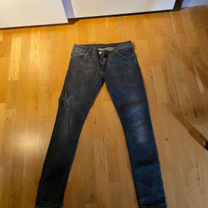 Svarta Nudie jeans - Säljer ett par svarta skinny jeans från Nudie Jeans med klassisk femficksdesign. Jeansen har en smal passform och är tillverkade i stretchig bomull för extra komfort. Perfekta för dig som gillar en stilren och modern look. Modell skinny lin. Knappt använda