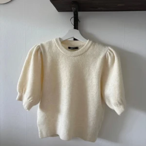 Puffärm stickad tröja från Gina Tricot - Superfin ljus stickad tröja från Gina Tricot med puffärmar och rund halsringning. Tröjan har kortare ärmar med volym och ribbade muddar vid hals och ärmslut. Perfekt för lager-på-lager och ger en söt vibe till din outfit.