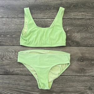 Ljusgrön bikini med sportig topp - Superfräsch ljusgrön bikini med sportig topp och höga trosor. Bikinin har en ribbad struktur som ger en trendig känsla och är tillverkad i mjukt syntetmaterial. Perfekt för strandhäng och poolparty i sommar!