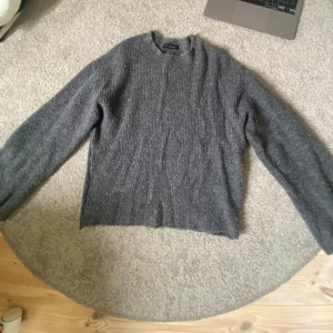 Grå stickad tröja från Dilvin - Mysig grå stickad tröja från dilvin med rund halsringning och lång ärm. Tröjan har en ribbad struktur och är perfekt för kyligare dagar. Enkel och stilren design som funkar till det mesta.