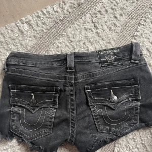 True Religion svarta jeansshorts - Snygga svarta jeansshorts från True Religion, modell Joey Cut-Off. Låg midja och är i storlek 26.