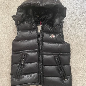 Moncler väst - Ania Hooded Down Gilet - Säljer min monclerväst då jag inte använder den längre!😇 Strlk 14+, jag är 18 och den passar bra på mig!  Modellen heter Ania Hooded Down Gilet och jag beställde den från Monclers egna hemsida :) Den är använd men har inga som helst skador eller skråmor, om man tvättar den en gång är den som ny! Nypriset var 5500 , säljer den för 3000☺️