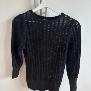 Svart stickad tröja med strukturmönster - Snygg svart stickad tröja med strukturmönster och rund hals. Tröjan har långa ärmar med breda muddar och en tightare passform. Perfekt att styla med jeans eller kjol för en cool look.