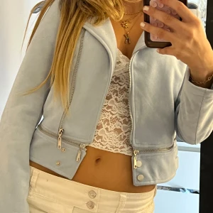 Ljusblå mocka bikerjacka Sateen - Säljer en ljusblå croppad bikerjacka från Sateen med coola dragkedjor och knappar. Jackan är i mjuk mocka-look och har klassisk krage. Perfekt för dig som vill sticka ut med en fräsch färg och snygg passform.