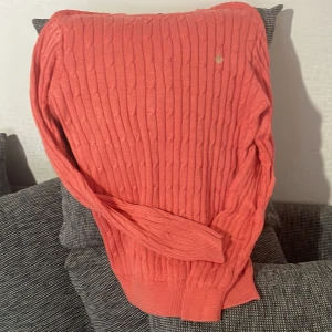 Korallfärgad stickad tröja Morris - Säljer en korallfärgad stickad tröja från Morris i merceriserad bomull. Tröjan har kabelstickat mönster, rund halsringning med beige detalj och långa ärmar. Perfekt för dig som gillar klassisk men ändå färgstark stil.