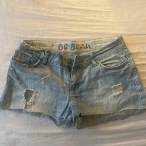 Ljusblå jeansshorts från Be Beau - Snygga ljusblå jeansshorts från Be Beau med slitna detaljer och råa kanter. Klassisk femficksmodell med bälteshällor och dragkedja. Perfekta för varma dagar och en avslappnad look.
