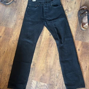 Svarta Levi's 501 Premium jeans 33/34 - Svarta Levi's 501 Premium jeans i klassisk rak modell. Jeansen har fem fickor, knappgylf och är tillverkade i robust denim. Snyggt minimalistiska och passar perfekt till sneakers eller boots. Ikonisk läderpatch bak i midjan och diskret Levi's-märke på bakfickan.