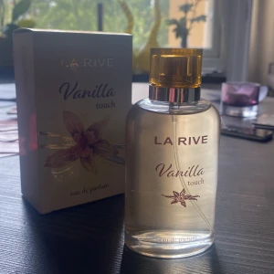 La Rive Vanilla Touch parfym - La Rive Vanilla Touch eau de parfum med söt vaniljdoft. Flaskan är genomskinlig med guldfärgat lock och stilren design. Kommer i en vit kartong med blomdekor och guldiga detaljer. Perfekt för dig som älskar varma, mjuka dofter. Nypris 90kr