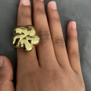  guldig blomring Stockholmstill - Stor och chunky ring i guldtonad metall med en cool, rundad blomformad design. Statement piece som verkligen drar blickarna till sig och ger en trendig vibe till din outfit.