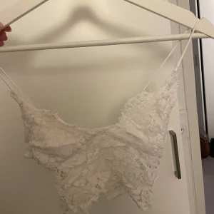 Vit spetsig linnetopp från Pieces - Supersöt vit linnetopp från Pieces med tunna axelband och spetsdetaljer över hela toppen. Toppen har en v-ringad form och är ärmlös, perfekt för en fräsch och somrig look. Spetsen ger en romantisk vibe och toppen är lätt och luftig.