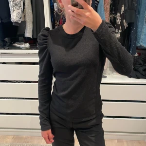 Svart långärmad topp med puffärm JDY - Svart långärmad topp från JDY i storlek XS. Mjuk bomullskänsla och normal passform, perfekt till jeans eller kjol!