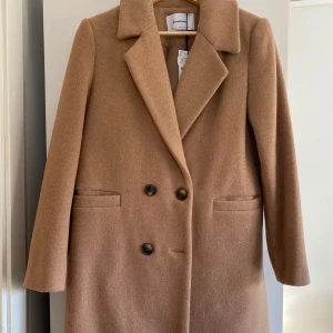 Beige lång kappa - helt ny - Snygg beige kappa från Zalando i ullblandning. Klassisk modell med dubbelknäppning, bred krage och raka fickor framtill. Perfekt för dig som vill ha en stilren och tidlös look under höst och vinter. Långärmad och med en rak passform. Längden syns inte så mycket på dessa bilder, men om man är intresserad kan jag skicka bättre bilder på kappan! 💕💕
