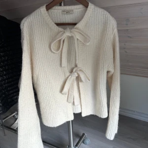 Vit stickad kofta med knyt från Gina Tricot - Supermysig vit stickad kofta från Gina Tricot med två knyt framtill. Koftan har långärmad design, ribbad struktur och en lite loose passform. Perfekt för lager-på-lager och chill höst- eller vinterstil.