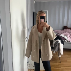 Beige kappa med dubbelknäppning - Säljer denna kappa då jag tycker den e lite för stor, är inte använd och är i bra skick. Perfekt för dig som vill ha en stilren och trendig look i höst och vinter.