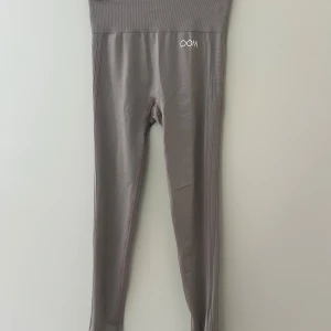 Grå/beige leggings från Drop of Mindfulness - Snygga grå leggings från Drop of Mindfulness med hög midja och ribbade detaljer upptill. Tillverkade i stretchigt material med 96% polyamid och 4% elastan för en tight och bekväm passform. Perfekta för träning eller chill dagar.