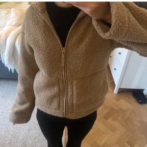 Beige teddyjacka med dragkedja - Mysig beige teddyjacka med dragkedja framtill. Perfekt för kyliga dagar med sin fluffiga och varma design. Jackan har en normal passform och långa ärmar. 450kr vid snabba köp