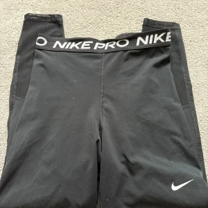 Svarta leggings från Nike - Snygga svarta Nike Pro leggings med elastisk midja och vit logga. Perfekta för träning med en tight passform som ger stöd och komfort. Tillverkade i ett mjukt och stretchigt material.