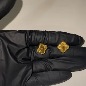 Eleganta örhängen i form av fyrklöver med guldfärgade detaljer. Helt oanvänd, köpt utomlands. Materialet är rostfritt stål med 18K guldplätering. 