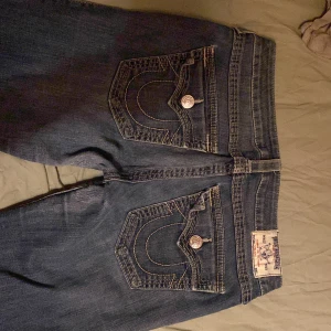 True Religion lowrise jeans  - Snygga blå jeans från True Religion med ikonisk broderad fickdetalj. Tillverkade i USA, dessa jeans har en klassisk femficksdesign och knappgylf. Bra skick, kontakta för frågor, använd gärna köp nu! pris kan diskuteras vid snabb affär