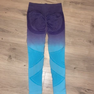 Lila och turkosa leggings - Snygga leggings i en cool ombre-design som går från lila till turkos. Tillverkade av 90% polyamid och 10% elastan för en stretchig och bekväm passform. Perfekta för träning eller en avslappnad dag. Har även en form där bak vilket formar din rumpa, det är storlek M men passar dig oavsett om du har XS eller XSS som mig. Med lila sömmar