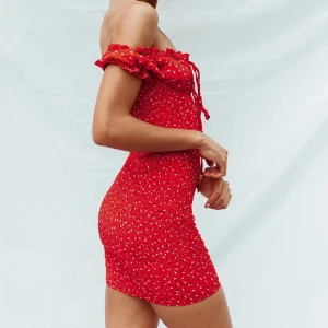 Röd blommig klänning - Nyskick. Endast använd en gång. Snygg röd kortklänning med blommigt mönster och offshoulder-design. Klänningen har volangdetaljer och snörning framtill för en söt look. 