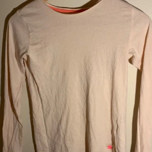 Beige långärmad tröja från H&M - Säljer en beige långärmad tröja från H&M i ekologisk bomull. Tröjan har en enkel design med en liten rosa stjärndetalj vid nederkanten. Perfekt för en avslappnad stil.
