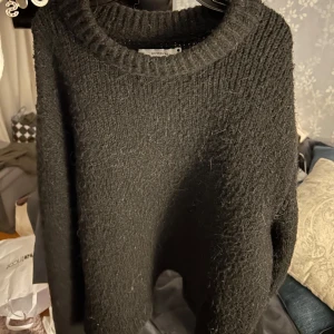 Svart stickad tröja från reversed - Mysig svart stickad tröja från reversed. Perfekt för kyliga dagar med sin varma och bekväma design. Tröjan har en rund halsringning och långa ärmar, vilket gör den till ett mångsidigt plagg i garderoben.