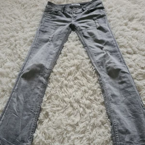 Lågmidjade grå bootcut jeans från Cindy H - Snygga grå jeans från Cindy H med slitna detaljer och en klassisk femficksdesign. De har en knapp och dragkedja framtill. Perfekta för en avslappnad stil och vardagsanvänding men kan självklart kläs upp. Midjemått: 38 cm + stretch, innerben: ca 79 cm!🩷