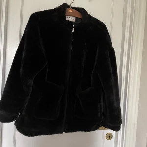Svart pälsjacka från NA-KD - Säljer en supermjuk och stilren svart pälsjacka från NA-KD. Jackan har en klassisk design med långa ärmar och två stora fickor framtill. 