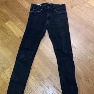 Svarta slim fit jeans från Jack & Jones - Snygga svarta slim fit jeans från Jack & Jones, modell Glenn. De har en klassisk femficksdesign och knappar i midjan. Perfekta för en stilren look.