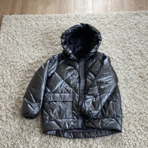 Svart/silvrig pufferjacka från Mohito - Snygg svart/silvrig pufferjacka från Mohito med quiltad design och huva. Jackan har en glansig yta och praktiska fickor framtill. Perfekt för kyligare dagar när du vill hålla stilen. 🖤