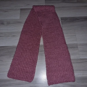 Rosa stickad halsduk - Säljer en mysig rosa stickad halsduk. Perfekt för att hålla värmen under kyliga dagar. Halsduken har en enkel och stilren design som passar till det mesta. Måtten är cirka 120 cm i längd och 15 cm i bredd.