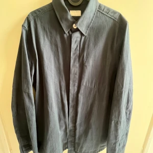 Mörkblå skjorta/jacka från Tiger of Sweden - Snygg mörkblå skjorta/jacka från Tiger of Sweden i storlek M. Skjortan har en klassisk krage och knappar framtill. Perfekt för en stilren look.