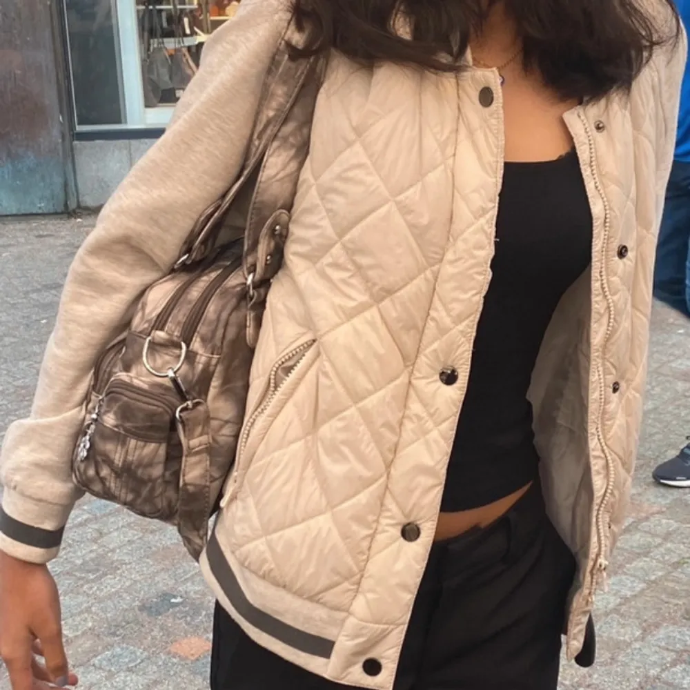 Säljer en beige quiltad bomberjacka från FB Sister. Jackan har gråa ärmar och ribbade muddar med svarta detaljer. Den har dragkedja och knappar framtill samt två fickor med dragkedja. Perfekt för en casual look!. Takit.