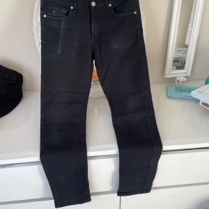 Svarta jeans från J. Lindeberg - Snygga svarta jeans från J. Lindeberg med klassisk femficksdesign och knappgylf. Perfekta för en stilren look..