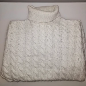 Vit stickad polotröja - Säljer en stilren vit stickad polotröja med klassiskt flätmönster. Tröjan har långa ärmar och en hög polokrage som håller dig varm under kyliga dagar. 