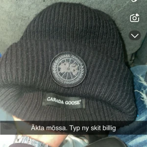 Svart ribbad mössa från Canada Goose - Säljer en svart ribbad mössa från Canada Goose med broderad logga framtill. Perfekt för kyliga dagar och ger en stilren look. Passar bra till både vardag och utomhusaktiviteter.