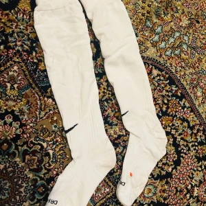 Vita Dri-FIT knästrumpor 39/ 40 - Säljer ett par vita Dri-FIT knästrumpor från Nike. De har en svart Nike-logga och är designade för att hålla fötterna torra och bekväma under träning. Perfekta för sportaktiviteter och har märkning för höger och vänster fot.