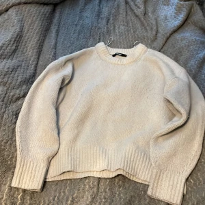 Vit stickad tröja från BikBok - Säljer en enkel och stilren vit stickad tröja från BikBok i storlek S. Tröjan har rund halsringning, långa ärmar och breda ribbade muddar vid ärmslut och nederkant. Perfekt för lager-på-lager under kyliga dagar.