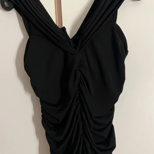 Fint festlinne - Säljer ett linne med djup v-ringning och snygg omlott-detalj. Linnet har draperad effekt framtill och är ärmlös, vilket ger en cool och trendig look. Perfekt för dig som gillar stilrena plagg med twist.