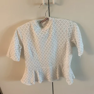 Vit spetsblus/topp med volang - Säljer en söt vit blus med spetsmönster och volang nertill. Blusen har korta ärmar och rund halsringning. Perfekt för dig som gillar romantisk stil!