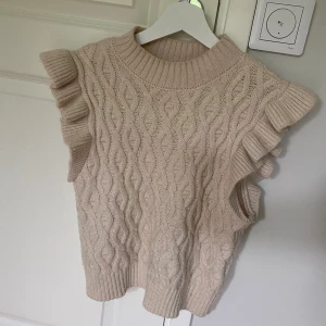 Volang tröja - Supersöt beige stickad tröja från Name It med volangdetaljer vid axlarna och ett fint kabelstickat mönster. Är i storlek 134-140 men väldigt stor i storleken. 