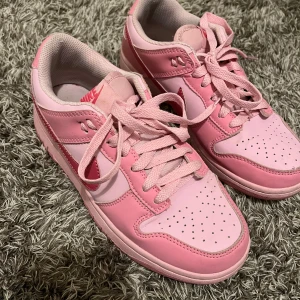 Nike Dunk sneakers i rosa och vitt - Säljer ett par Nike Dunk sneakers i olika nyanser av rosa med vita detaljer. Skorna har klassisk snörning, perforerad tå och rosa Nike-logga på sidan. Perfekta för dig som vill sticka ut med färg på fötterna!