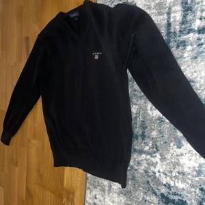 Svart stickad tröja från Gant - Klassisk svart stickad tröja från Gant med v-ringad hals och diskret logga broderad på bröstet. Perfekt för lager-på-lager och passar till många olika stilar. Storlek XS men funkar på S bara att den kan bli lite kort vid midjan. Dåliga bilder så skriv om du vill se mer