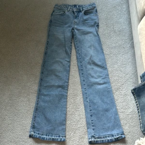 Ljusblå bootcut jeansbyxor - Ljusblå jeansbyxor i bootcut-modell med klassiska fem fickor och silverfärgade knappar. Byxorna har normal passform och är i kort längd (short). Perfekta för dig som gillar en retroinspirerad look.