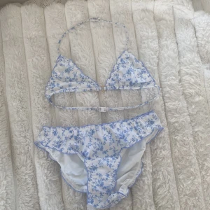 Blåvit blommig bikini - Supersöt bikini från Gina Tricot i vitt med blått blommönster. Överdelen är ovadderad. Aldrig använd. Plastlappen på underdelen är kvar. Perfekt för sommardagar på stranden!💘