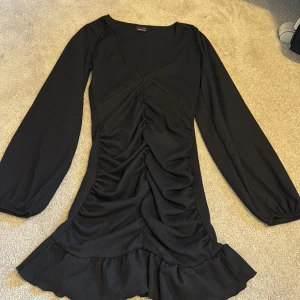 Svart omlottklänning med volang från Gina Tricot - Säljer en svart långärmad klänning från Gina Tricot i storlek XXS. Klänningen har v-ringning, rynkade detaljer framtill och volang nertill. Perfekt för dig som gillar en feminin och trendig stil.