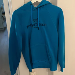Blå hoodie från Peak Performance - Säljer en blå hoodie från Peak Performance med broderad logga på bröstet. Tröjan har huva med dragsko och en stor magficka framtill. Perfekt för en avslappnad stil. Pris kan diskuteras 